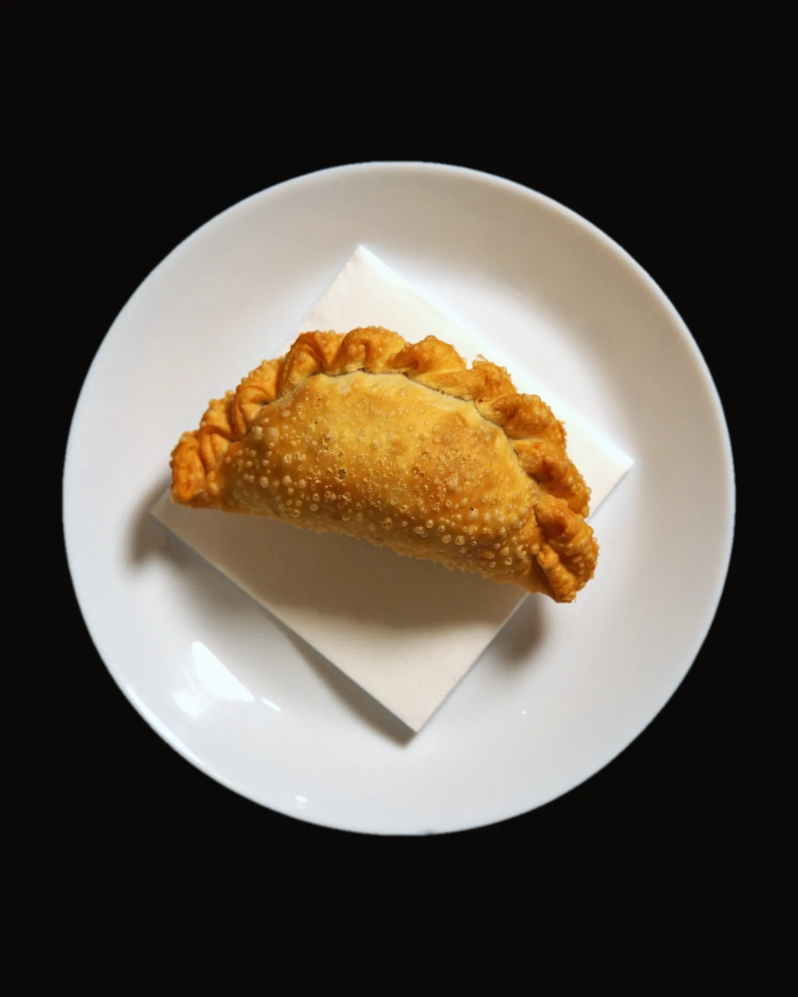 Empanada frita con el repulgo hecho a mano, en un plato blanco, vista desde arriba