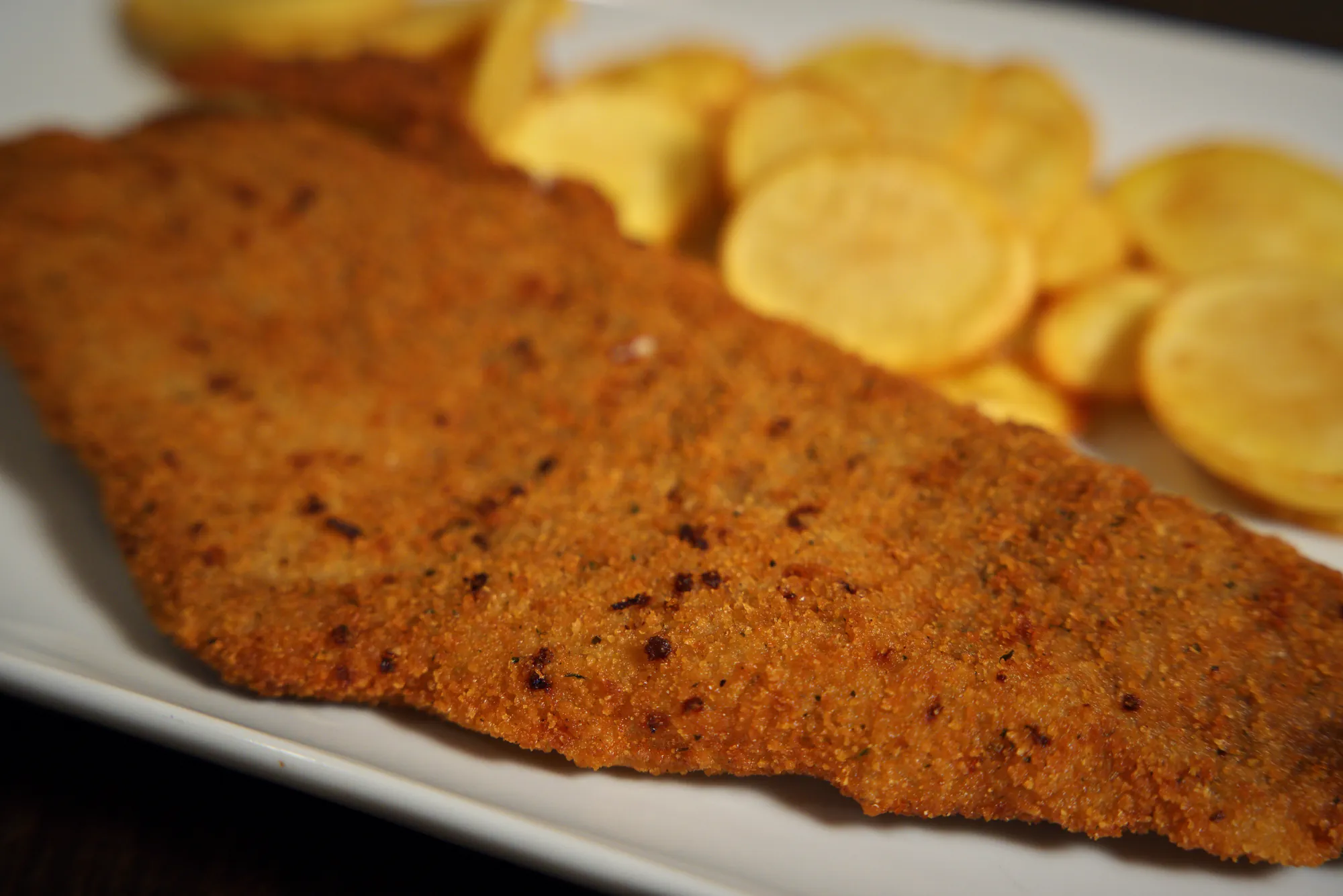 Primer plano del empanado dorado de una milanesa con papas fritas caseras