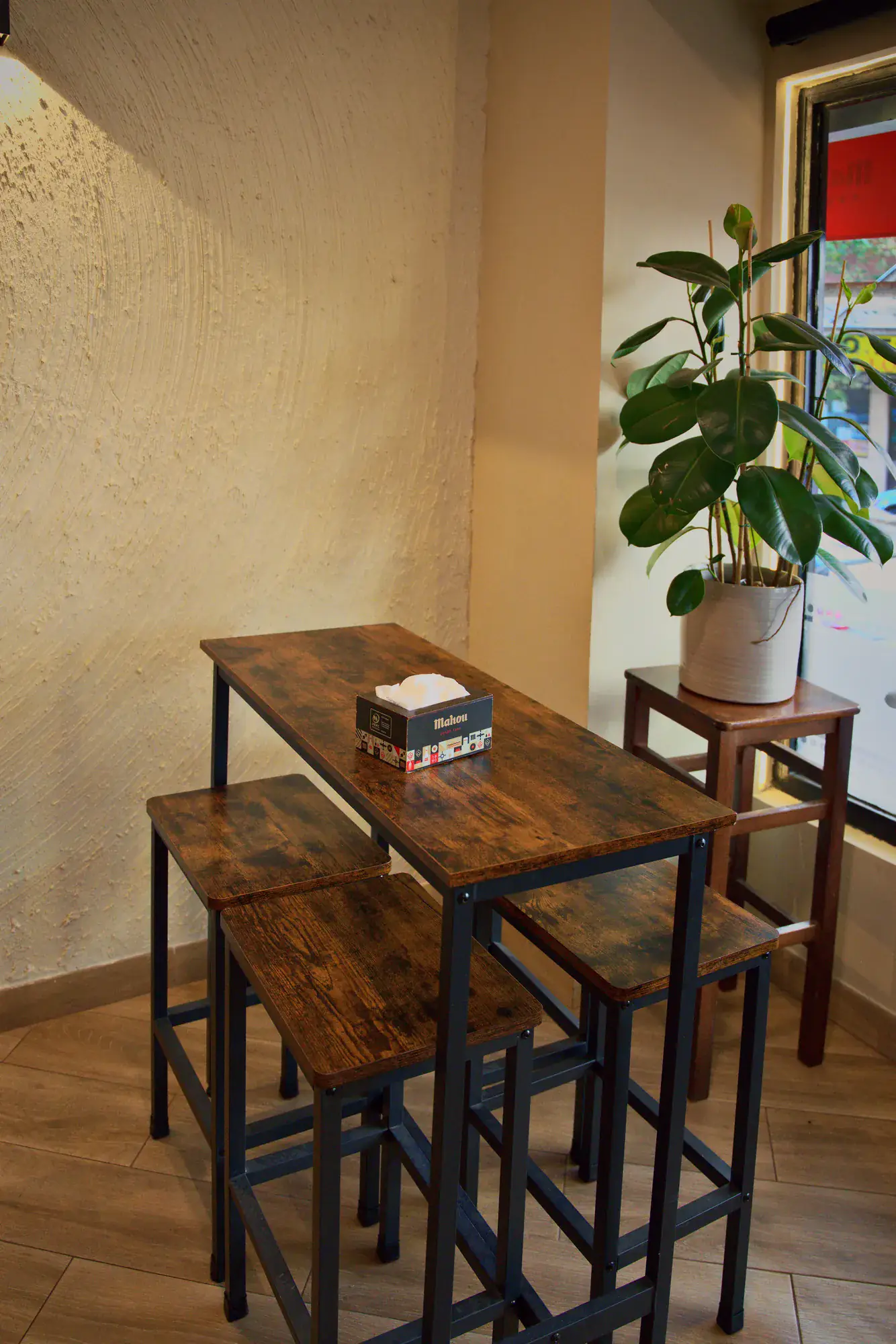 Mesa alta de madera junto al ventanal, con una planta y la calle al fondo